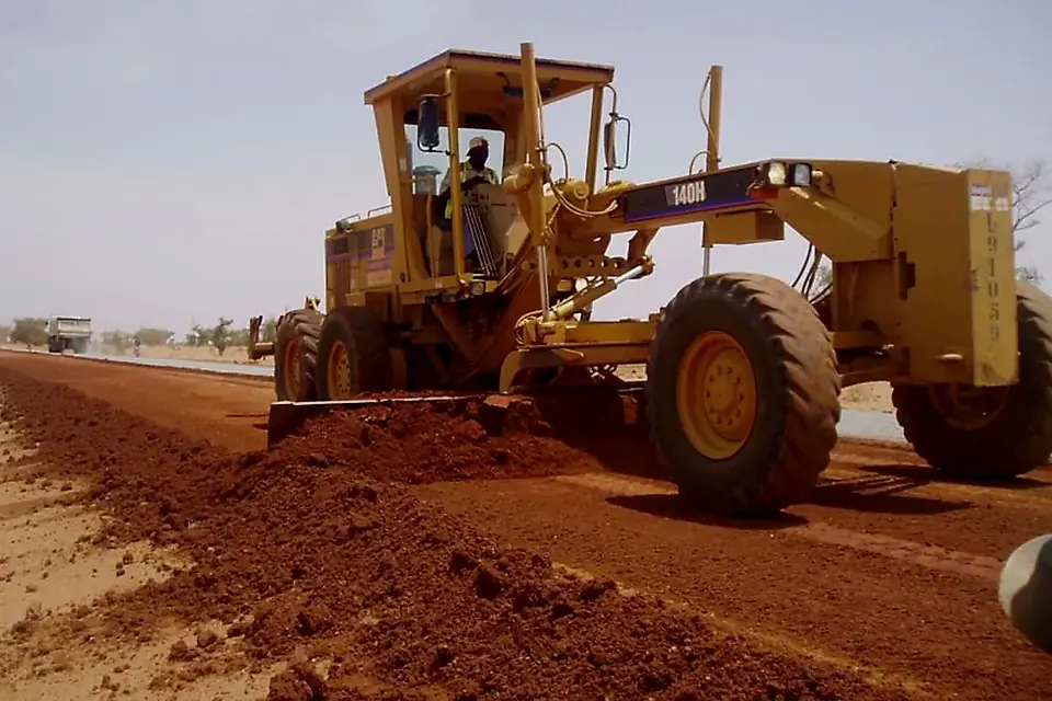Motoniveladora amarela a regularizar o leito de uma estrada de terra vermelha